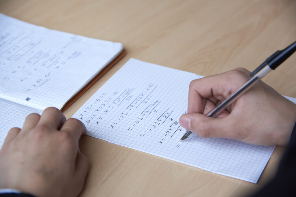 picture of a hand with paper and pen doing Maths problems